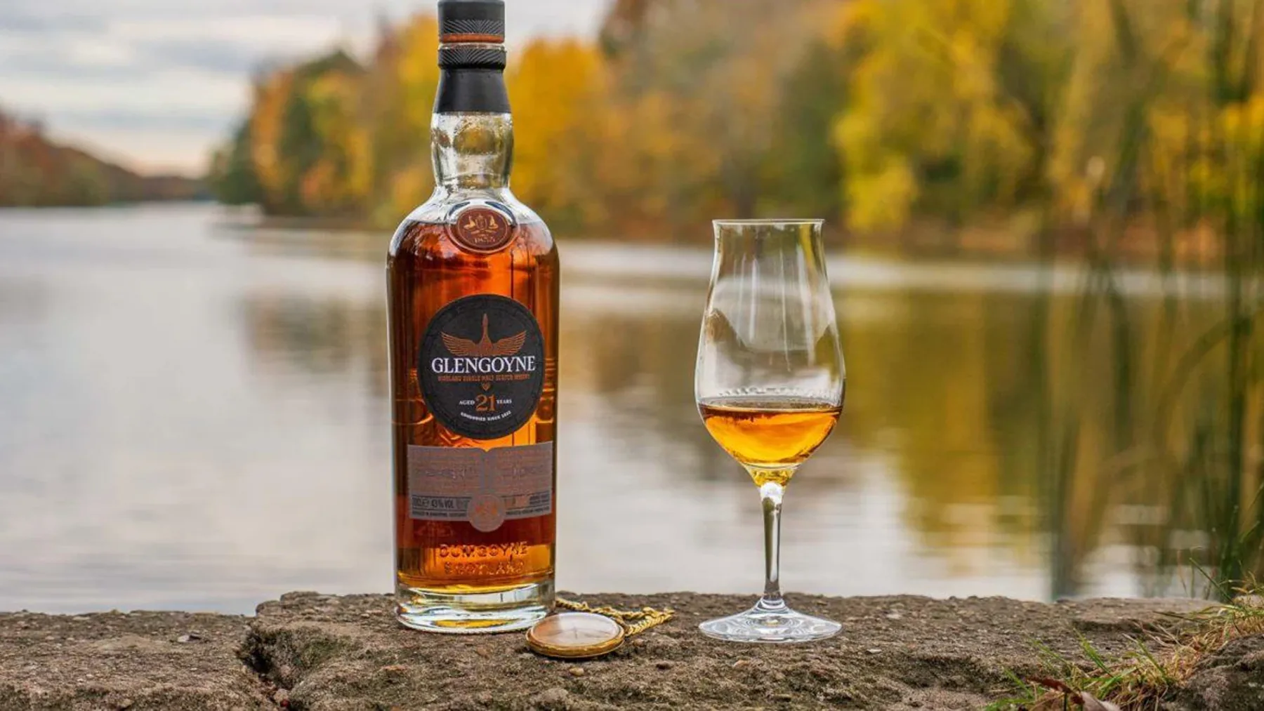 Ahşap masa üzerinde duran perdeli karton hediye kutusu ve Glengoyne 21 viski şişesi