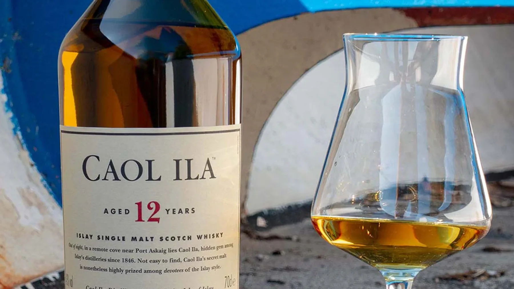 Ahşap masa üzerinde duran Caol Ila 12 viski şişesi ve kadehi