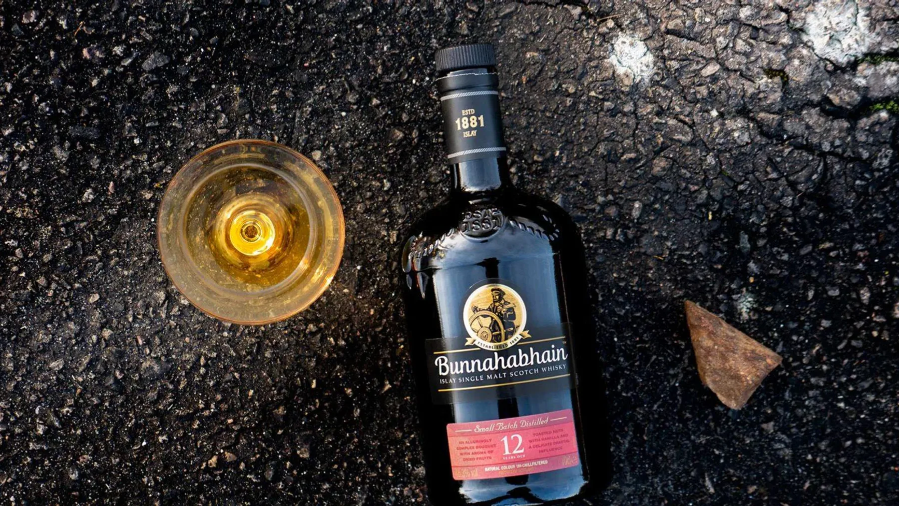 Eski ve yeni Bunnahabhain 12 viski şişeleri yan yana dururken kadehteki kehribar tonlu içki